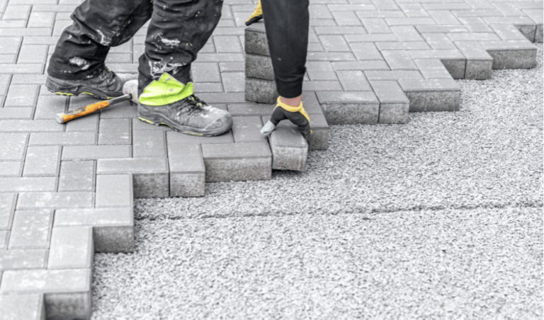 Professional brick paver installation in progress, featuring a worker laying brick pavers for a patio or walkway.