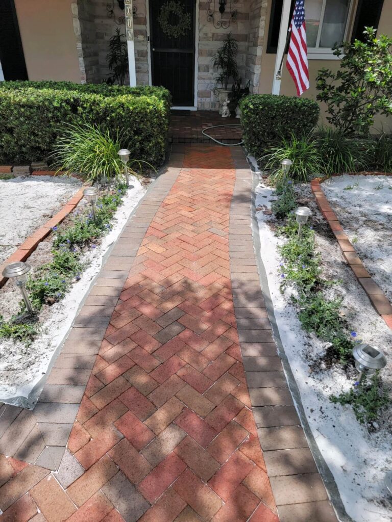 A brick walkway leads to a house adorned with a flag, set against a driveway in Lakeland, FL.